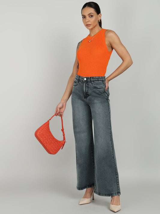 A woman wearing an orange sleeveless top and high-waisted grey wide-leg jeans from OMG Jeans, accessorized with a matching orange handbag and nude heels.