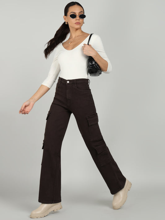 A stylish woman wearing brown cargo pants from OMG Jeans, paired with a white fitted top, beige chunky boots, black sunglasses, and a black handbag, striking a confident pose against a neutral background.