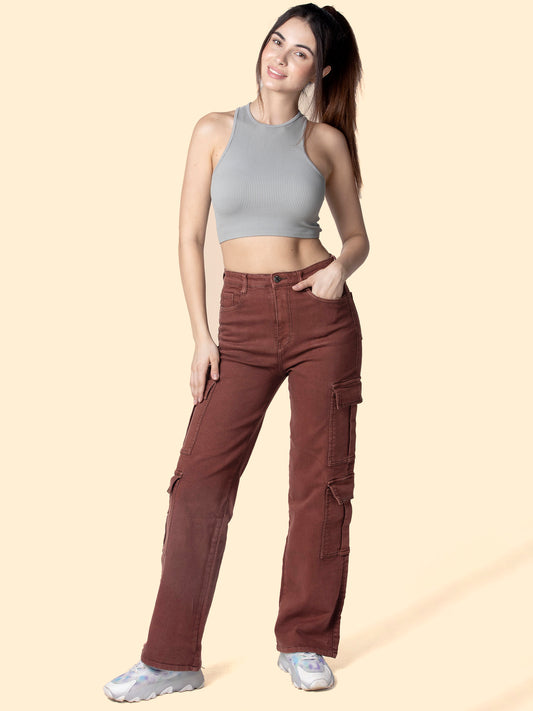  A stylish woman wearing maroon cargo pants from OMG Jeans, paired with a gray sleeveless crop top and white chunky sneakers, posing confidently against a light beige background.